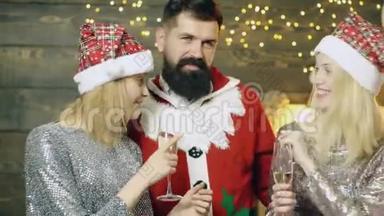 穿着桑塔服装的大胡子男人和戴着<strong>新年帽</strong>子的两个女孩`在圣诞节喝香槟，玩得开心。 <strong>新年</strong>`